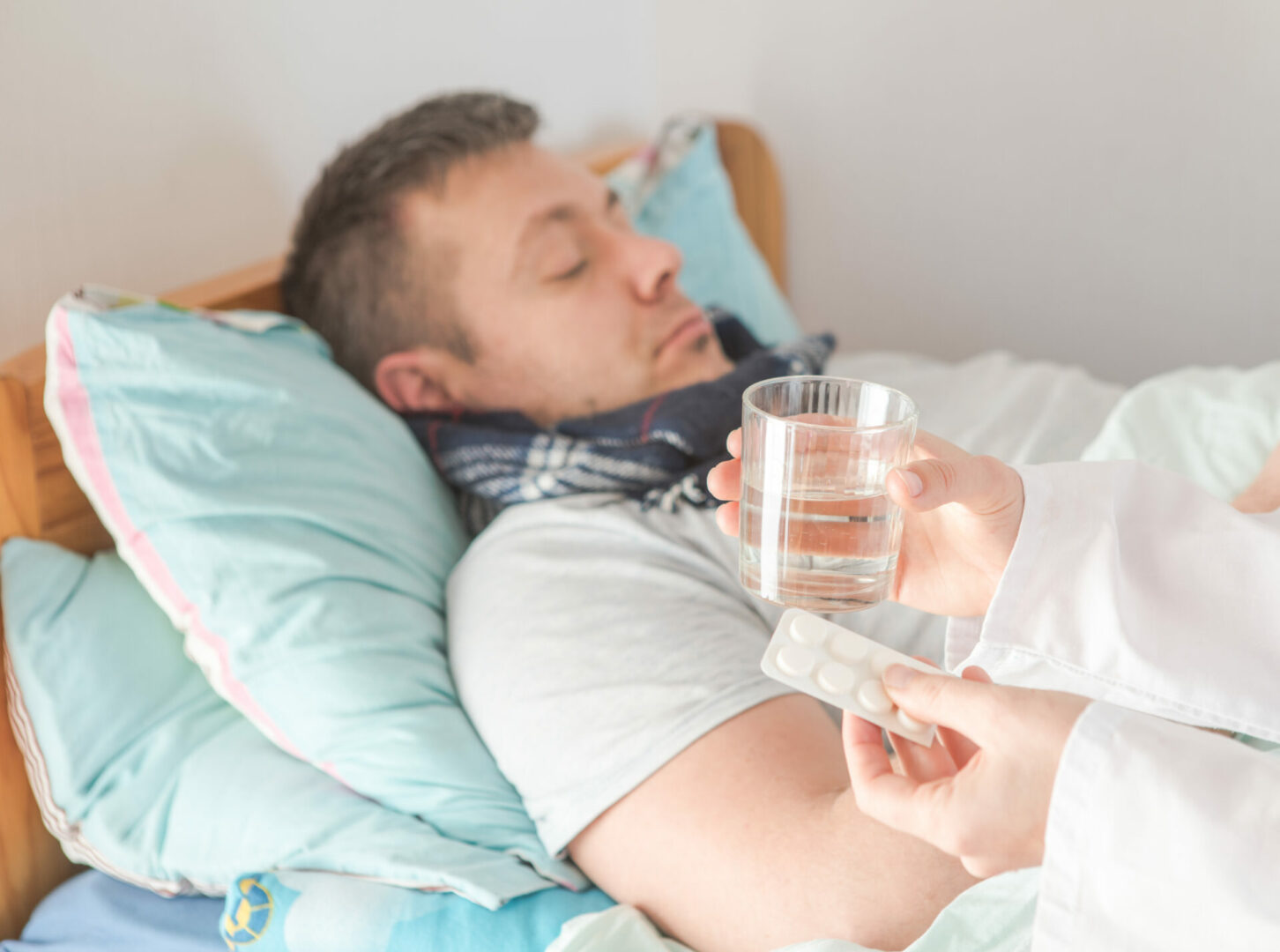 Nurse giving pills and glass with water to a male patient lying